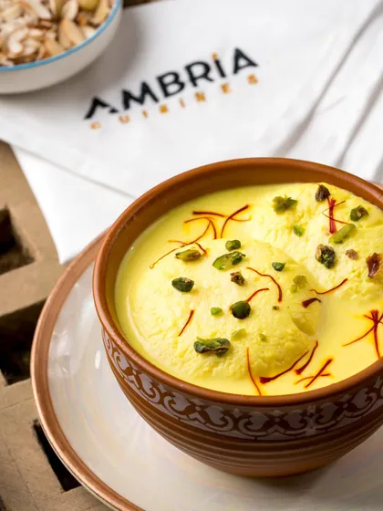 The royal Kesari Rasmalai. Soft cheese dumplings soaked in saffron-infused milk, garnished with pistachios. A timeless Indian dessert for a luxurious finish.