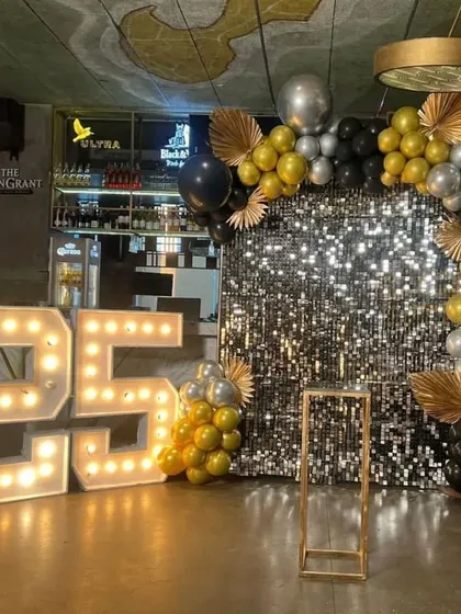 Let's get the party started with a glamorous photo corner. This 25th birthday setup features a shimmering sequin wall, a bold balloon arch in black, gold, and silver, and large marquee numbers for a high-impact look.