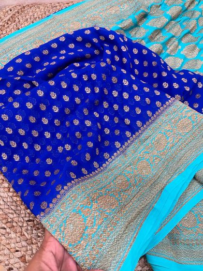 A royal blue pure Banarasi Kadi georgette saree with a bright turquoise border. The gold butis on the blue body create a beautiful, shimmering effect.