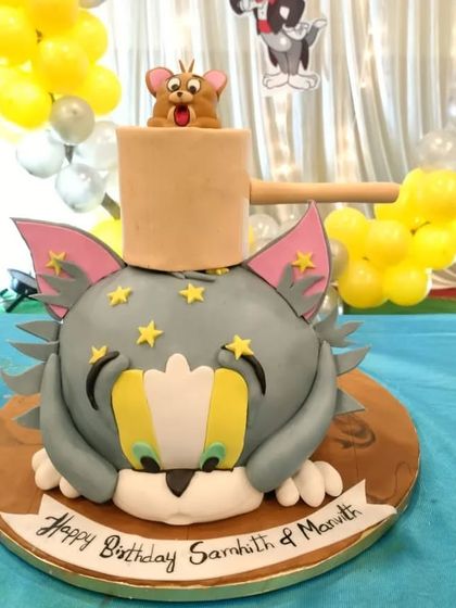 A playful and highly detailed 3D sculpted Tom and Jerry cake. This fun design captures the classic cartoon chase, with Jerry popping out of a mallet on top of Tom's head.