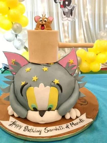 A playful Tom and Jerry cake, sculpted to look like Tom's head with Jerry popping out of a mallet. It's a fun and nostalgic choice for all ages.