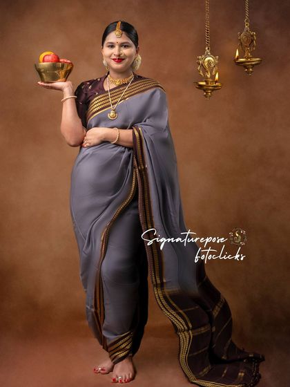 A full-length portrait in a grey saree, showcasing the unique draping style and traditional hanging lamps.
