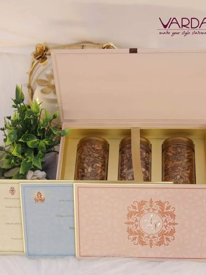 This elegant invitation hamper is designed to hold both the invitation cards and jars of dry fruits. The soft pink box with a gold monogram offers a tasteful and hospitable way to invite guests to your celebration.
