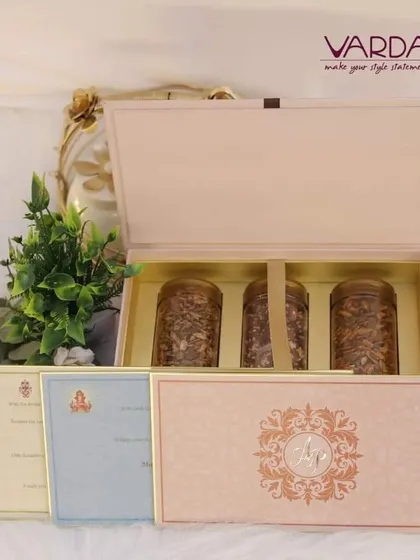 This elegant gift box in a soft peach hue is designed to hold three jars of premium dry fruits or other gourmet items. It is accompanied by a set of beautifully designed wedding cards for different functions.