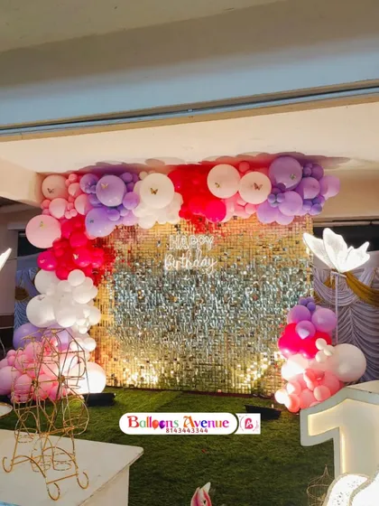 A glamorous party setup with a gold sequin wall and a pink, purple, and white balloon arrangement. The glowing butterfly props add a touch of whimsy.