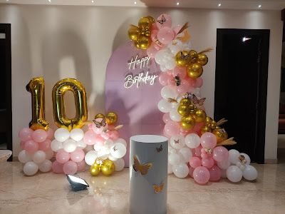 A chic 10th birthday setup with a pink, white, and gold balloon arrangement against a lilac arch backdrop. The decor includes large foil number balloons and a themed plinth, creating a stylish look.