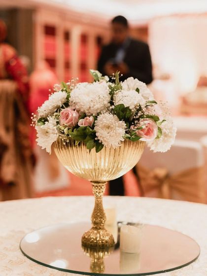 An elegant table centerpiece featuring white and pink flowers in a golden chalice. This classic arrangement adds a touch of sophistication to the reception decor.