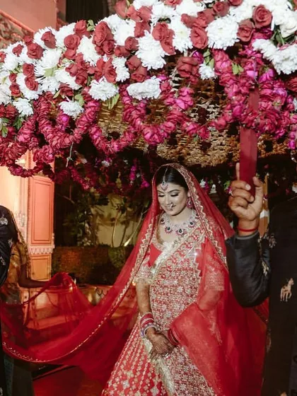 The bride's entry under a beautiful floral 'phoolon ki chadar'. This traditional moment is elevated with a lush arrangement of red and white flowers, making it a truly special part of the ceremony.