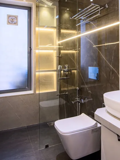 A modern bathroom featuring a glass-enclosed shower with built-in, backlit shelving for toiletries. The combination of dark floor tiles and lighter wall tiles creates a balanced and sophisticated look.