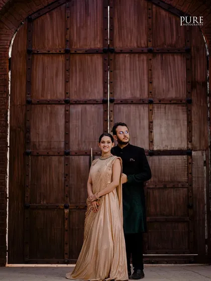 Dheeraj and Navdeep pose in front of a massive, rustic wooden door, giving their pre-wedding portrait a grand and historic feel. Her golden gown and his dark sherwani add to the regal look.