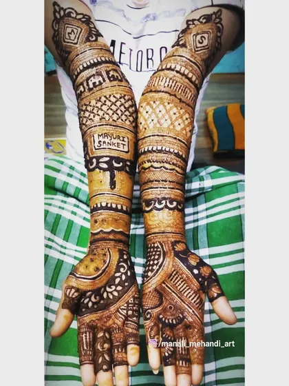 The couple's names, 'Mayuri' and 'Sanket', are integrated into this full-arm bridal mehandi. The design uses bold lines and dense patterns for a striking effect.