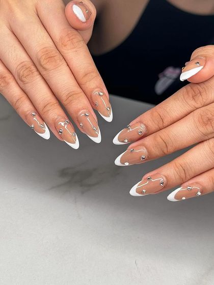 A modern French manicure with a nude base, white tips, and scattered silver bead accents.