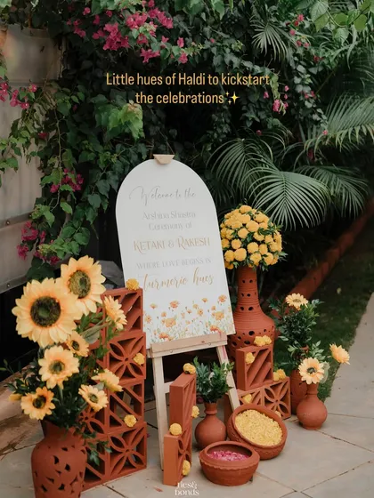 Welcome to the Haldi! We styled this entrance with rustic terracotta pots, cheerful sunflowers, and a custom welcome sign to set a warm and inviting tone for the "turmeric hues" celebration.