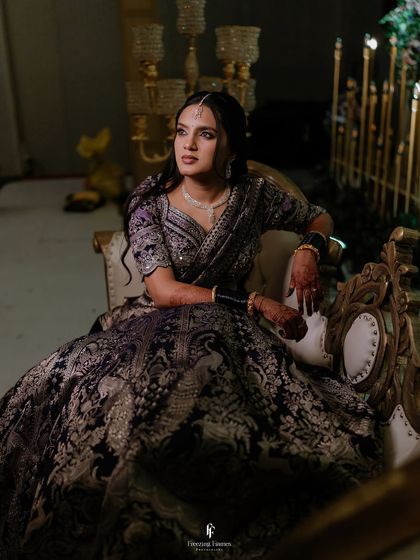 A dramatic portrait of the bride in a dark, heavily embroidered lehenga, looking away with a thoughtful expression.