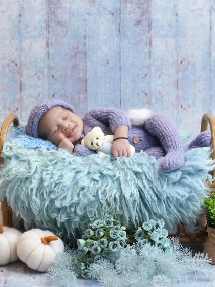 A sweet bunny-themed setup with a baby in a lavender knit outfit, sleeping on a fluffy blue bed. The white pumpkins add a touch of rustic charm.