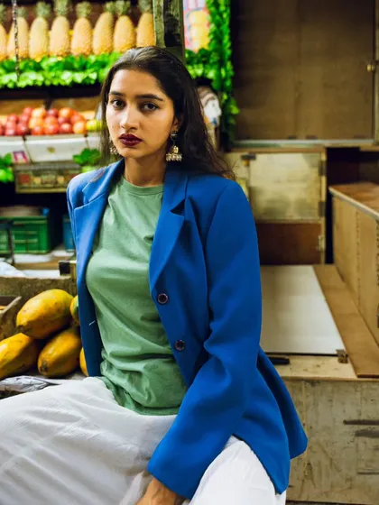 A relaxed pose in a fruit market. The background filled with pineapples and papayas adds a tropical, colorful vibe to this urban fashion shoot.
