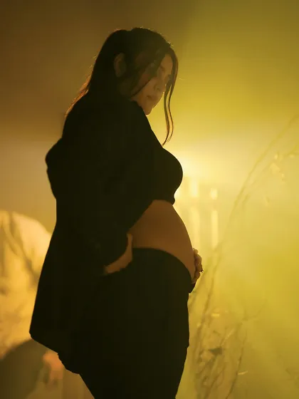 A modern and edgy studio portrait. The mother-to-be is dressed in a stylish black suit, her baby bump visible, creating a powerful and contemporary image of motherhood.