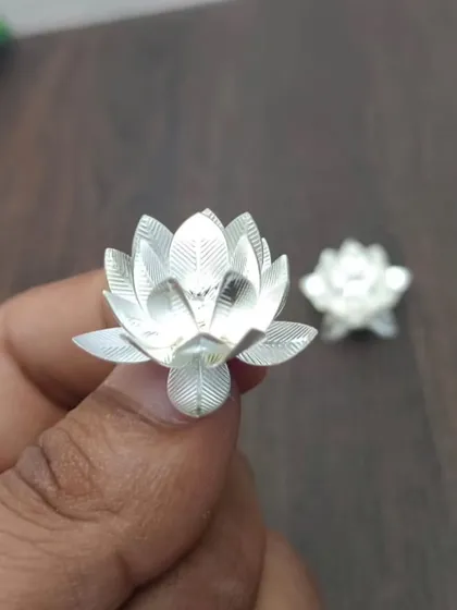 A hand-held view of a silver-finish German silver lotus flower, showcasing its delicate and realistic design.