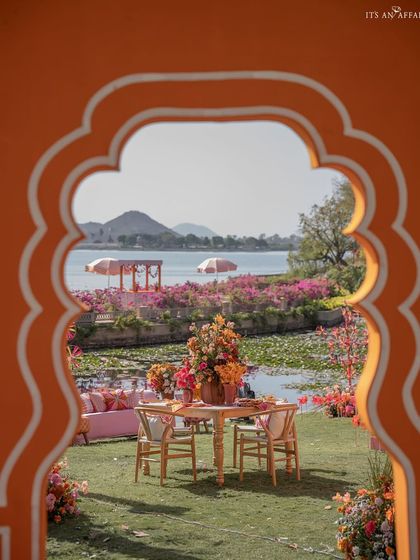 A view of the lakeside seating, framed through a traditional Rajasthani arch. The decor's bright colors pop against the serene blue of the water and sky.