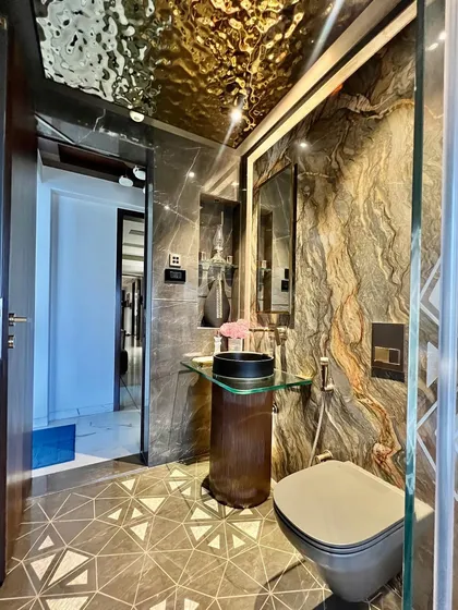 Continuing the tour of this beautiful bathroom, this angle shows the interplay of the geometric floor tiles, the dark marble walls, and the reflective gold ceiling, creating a space that is rich in texture and pattern.
