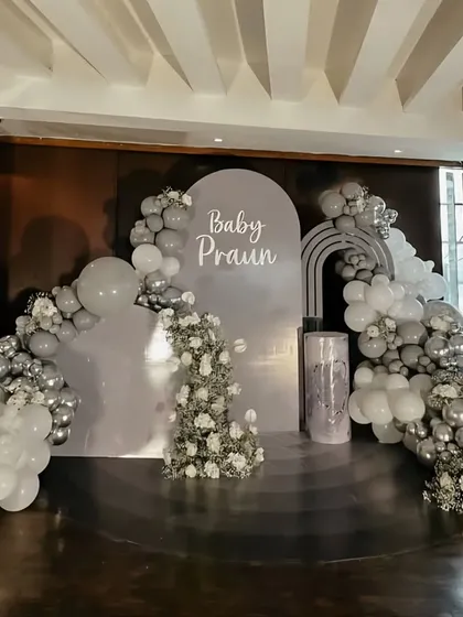 An elegant and sophisticated baby shower for "Baby Praun" in a silver and grey monochrome palette. The setup features a full stage with arched backdrops and beautiful cascades of balloons and white flowers.