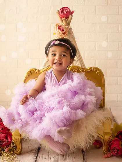 A happy birthday girl with a big smile, sitting on her golden chair in a whimsical, light-filled setup.