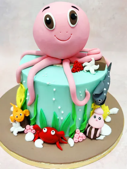 This Octopus Theme Cake features a cheerful pink octopus amidst a lively group of sea friends, including a crab, fish, and snail.