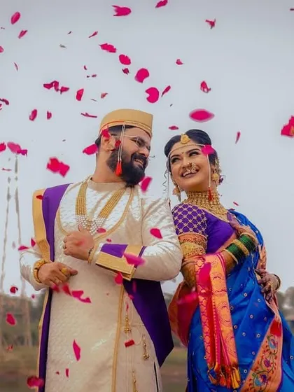 A shower of rose petals rains down on the happy couple. The vibrant colors of their traditional Maharashtrian outfits pop against the sky.