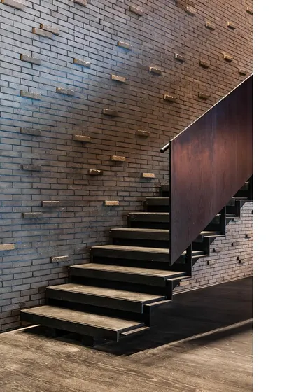 A staircase at the BCG office is framed by a textured brick wall where bricks protrude at intervals. This detail adds a layer of craftsmanship and tactile interest to a functional element.