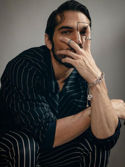 A close-up shot focusing on hand gestures and accessories. The styling incorporates multiple rings and a bracelet to complement the pinstripe suit and add a layer of detail to the character.