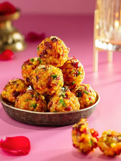 A pyramid of delicious Boondi Ladoo, a classic Diwali sweet, for the Marriott campaign. The vibrant pink background and scattered rose petals create a festive and joyful mood, highlighting this traditional favorite.