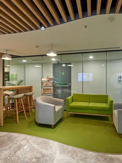 A green-themed lounge area with a curved green carpet that defines the space. The organic shape of the ceiling cutout and carpet creates a natural, flowing feel.