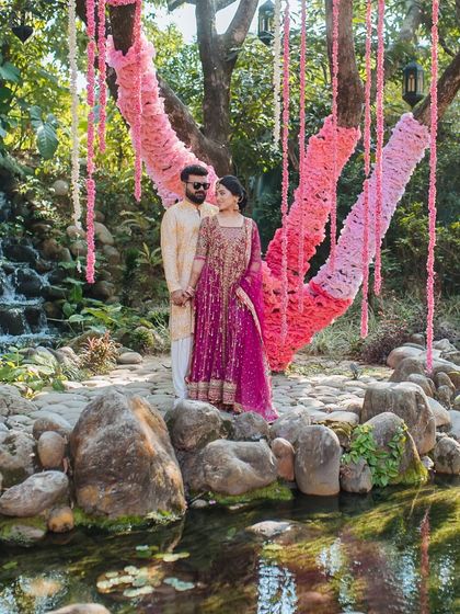 A beautiful portrait of the couple at their Haldi ceremony in Jim Corbett, standing by a tree decorated with pink floral hangings.