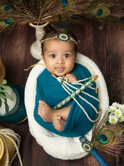 A sweet newborn portrait with a Janmashtami theme, complete with a peacock feather headband and a tiny flute.