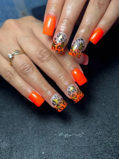 A bold and trendy set of square-shaped nails featuring a neon orange base with leopard print French tips. The gold foil accents add an extra touch of glamour.