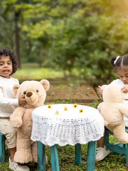 Twin toddlers enjoying a teddy bear tea party outdoors. Themed shoots like this are a great way to capture children's imaginations and personalities.
