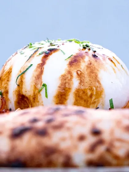 A side-profile of the burrata on the pizza, highlighting its height and the beautiful char marks from the grill. It builds anticipation for the cut.