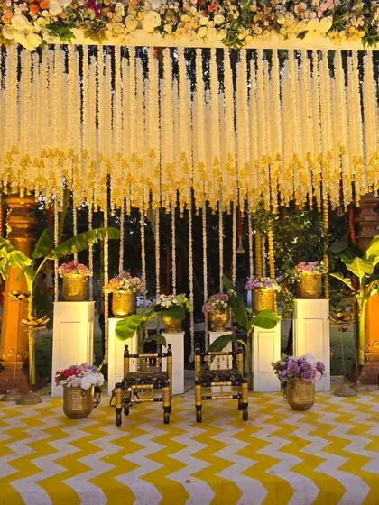 A close-up of the South Indian Haldi stage. You can see the detail in the hanging floral strings (latkans), the brass pots filled with flowers, and the traditional seating for the couple.