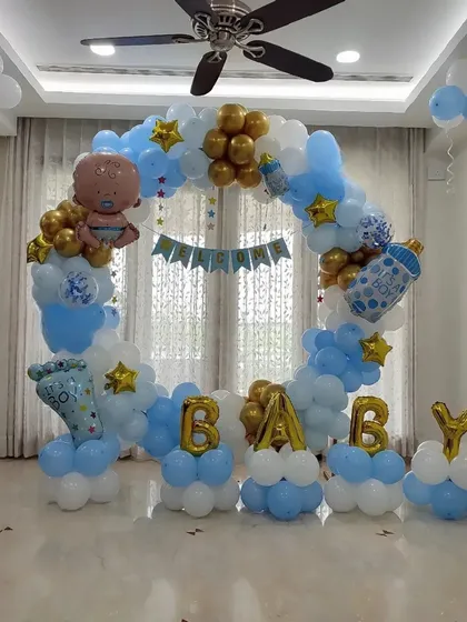 A classic 'Welcome Baby' decoration for a baby boy. This circular balloon arch in blue, white, and gold is filled with fun foil balloons like a baby bottle and footprint, creating a perfect photo spot at home.