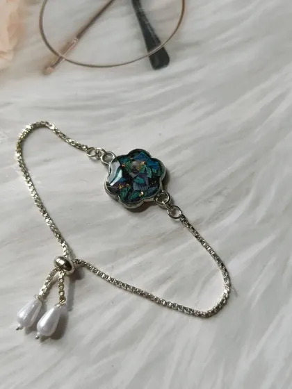 A close-up of the adjustable silver bracelet with a flower charm made from preserved orchids. The pearl details on the clasp add an elegant touch.