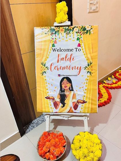 The personalized 'Welcome to Haldi Ceremony' easel, decorated with marigold flowers.
