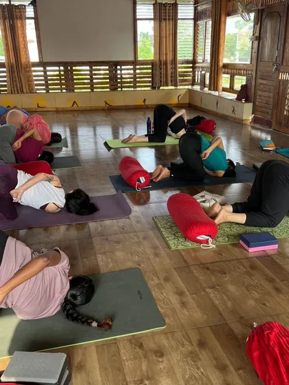 A class of students in Karnapidasana (Ear Pressure Pose), a deep forward bend that calms the nervous system.