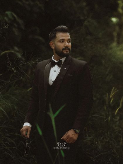 A stylish portrait of the groom in a lush, dark green environment, creating a moody and sophisticated look.