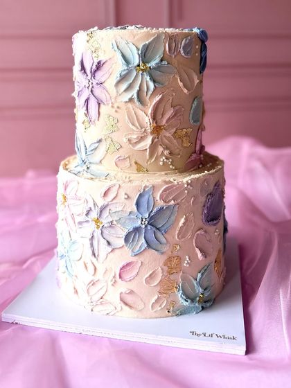 A two-tiered cake covered in beautiful, textured buttercream flowers in a palette of pastel blues, pinks, and yellows. This design is like a painting you can eat.