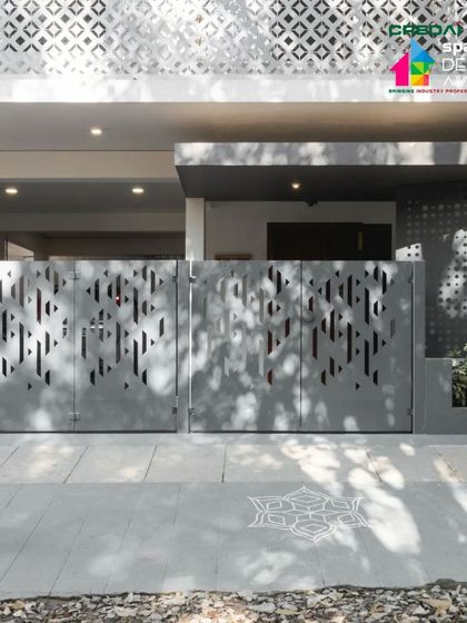 The main gate of the '10x10 Residence', featuring a modern, abstract perforated pattern that complements the jaali screen on the facade. A traditional Rangoli pattern is subtly etched into the pavement.