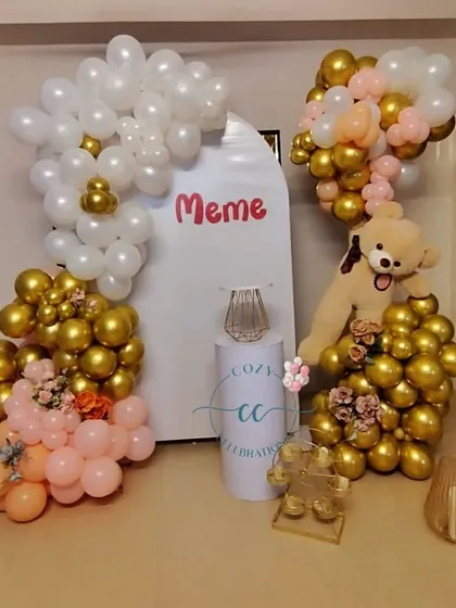An elegant and sweet setup for a baby celebration. This decor uses a clean white and gold color palette with touches of soft pink, complete with a plush teddy bear for a cute finish.