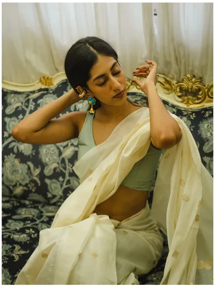 A graceful and serene portrait. The model's pose, with her eyes closed and hands adjusting her earring, feels like a quiet, personal moment. The elegant setting and soft lighting enhance the timeless quality of the image.