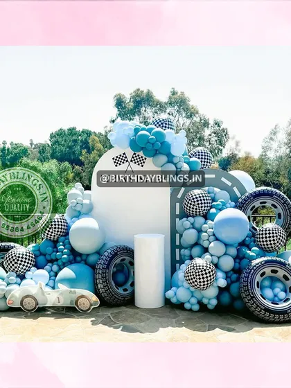 An outdoor race car party with a "First Lap" theme. The setup is loaded with details, including real tires, checkered balloons, and a vintage race car cutout.