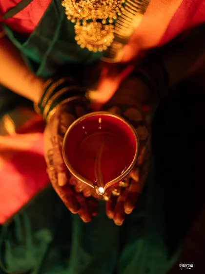 A detailed top-down shot focusing on hands holding a lit diya. This image symbolizes the light and hope of Diwali, with the intricate henna and traditional jewelry adding to the festive feel.