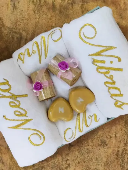 A complete wedding gift set for the bride and groom. It has everything: customized name towels, 'Mr' and 'Mrs' hand towels, golden heart-shaped soaps with initials, and two luxury candles.
